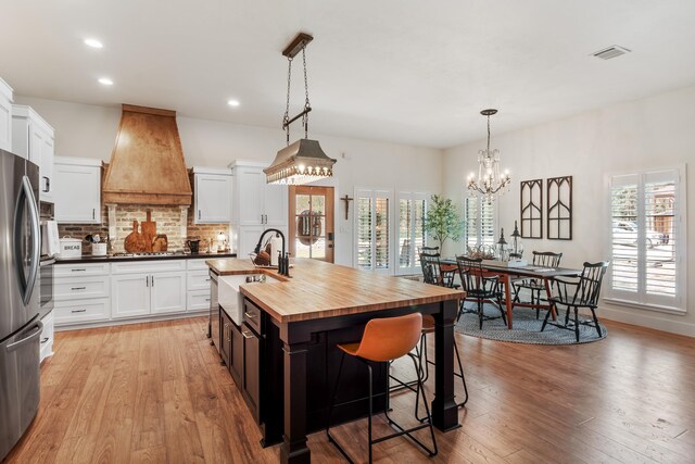 kitchen featuring wood counters, custom range hood, white cabinetry, and an island with sink