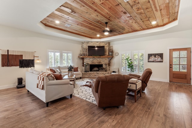 living room featuring a raised ceiling, hardwood / wood-style flooring, ceiling fan, a fireplace, and wood ceiling