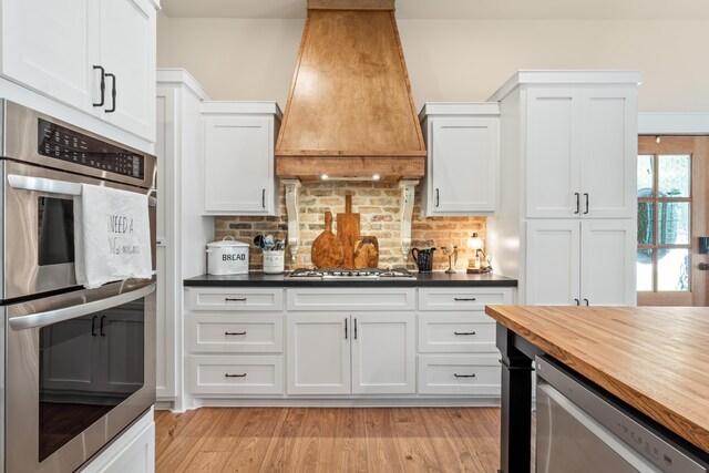 kitchen featuring custom exhaust hood, white cabinetry, butcher block counters, and appliances with stainless steel finishes