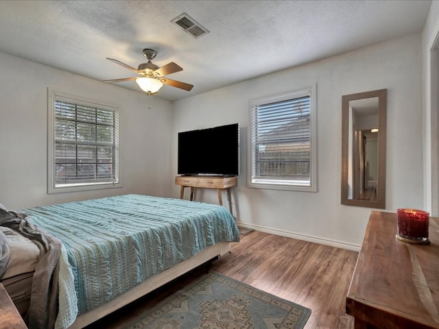 bedroom with multiple windows, ceiling fan, a textured ceiling, and hardwood / wood-style flooring