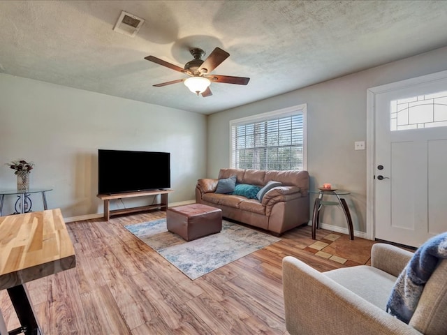 living room featuring ceiling fan, light wood-type flooring, and a textured ceiling