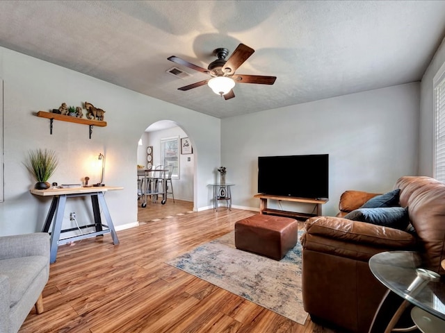 living room with ceiling fan, light wood-type flooring, and a textured ceiling