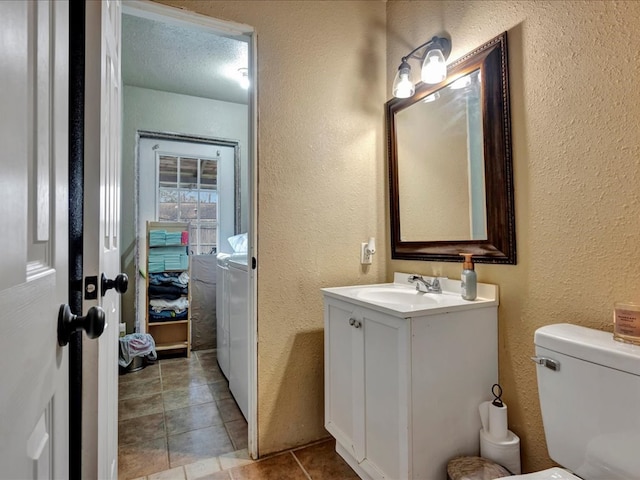 bathroom with vanity, a textured ceiling, toilet, and washing machine and clothes dryer