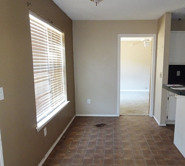 unfurnished dining area with a ceiling fan and baseboards