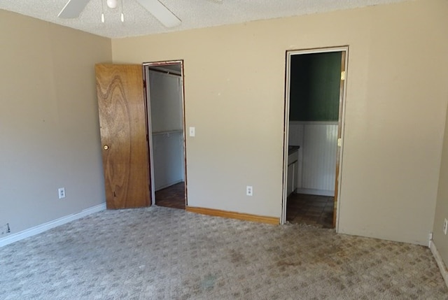 unfurnished bedroom featuring a textured ceiling, a spacious closet, a ceiling fan, and carpet flooring