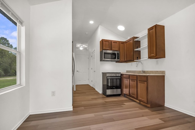 kitchen with appliances with stainless steel finishes, vaulted ceiling, light hardwood / wood-style flooring, and plenty of natural light