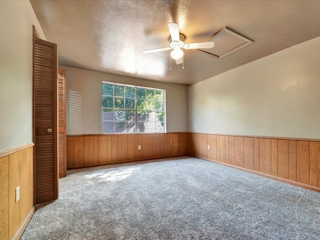 carpeted empty room featuring ceiling fan, a textured ceiling, and wooden walls