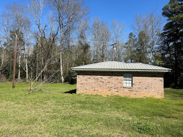 view of side of property with a lawn, brick siding, and metal roof