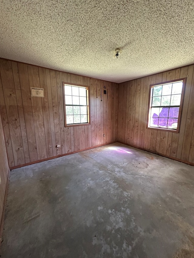 empty room featuring plenty of natural light, a textured ceiling, concrete flooring, and baseboards