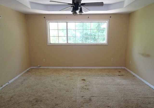 carpeted empty room with a tray ceiling, ceiling fan, and a healthy amount of sunlight