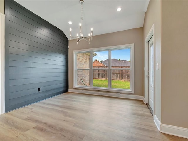 unfurnished dining area with a chandelier, vaulted ceiling, and light hardwood / wood-style flooring