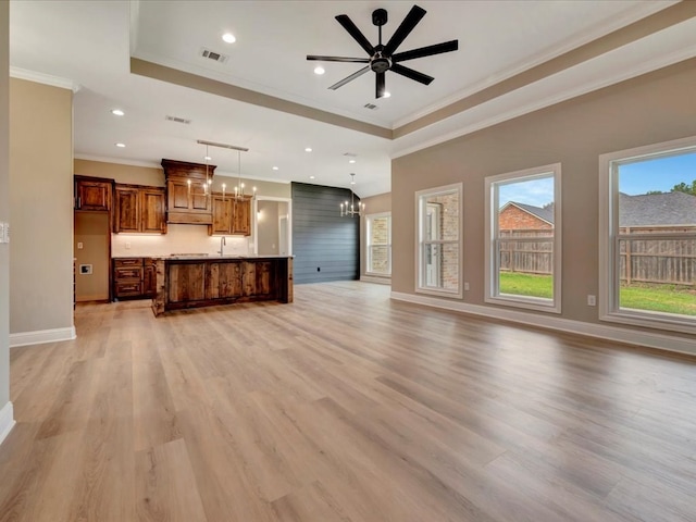 unfurnished living room featuring ceiling fan with notable chandelier, light hardwood / wood-style floors, a raised ceiling, and crown molding