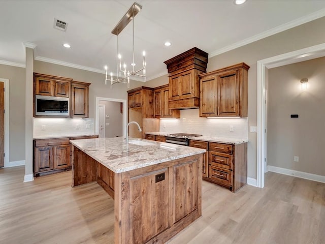 kitchen featuring light wood-type flooring, light stone counters, stainless steel appliances, a notable chandelier, and an island with sink