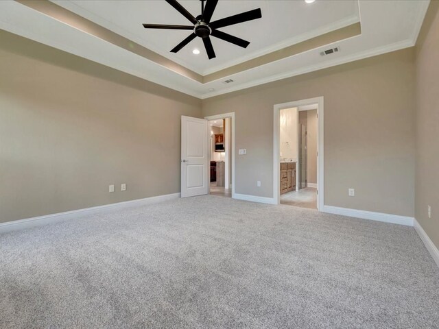 unfurnished bedroom with ensuite bath, light colored carpet, a raised ceiling, ceiling fan, and crown molding