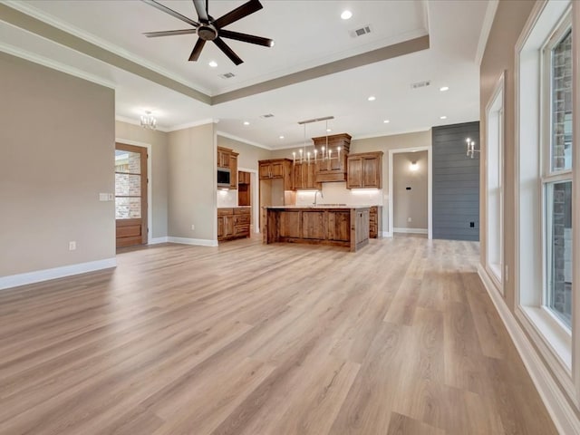 unfurnished living room featuring ceiling fan with notable chandelier, a raised ceiling, crown molding, sink, and light hardwood / wood-style floors