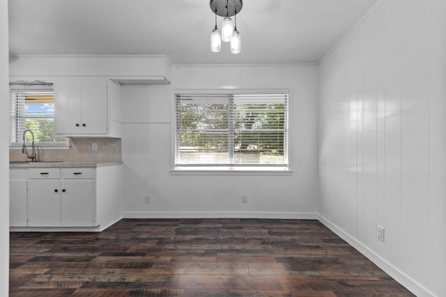 unfurnished dining area featuring dark wood-style floors, baseboards, a sink, and crown molding