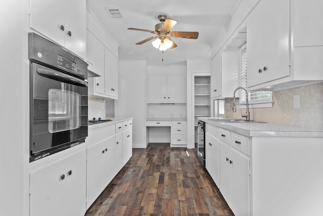 kitchen with dark wood-style flooring, visible vents, oven, ceiling fan, and a sink
