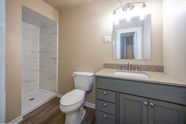 bathroom with hardwood / wood-style flooring, vanity, toilet, and tiled shower