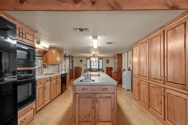 kitchen with sink, a center island with sink, black appliances, and light wood-type flooring