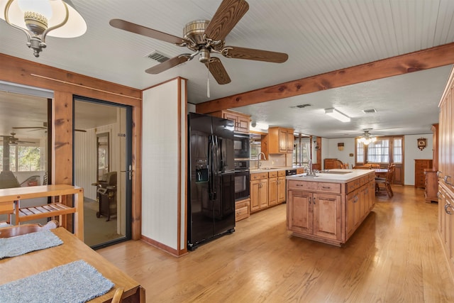 kitchen with black appliances, a center island with sink, sink, ceiling fan, and light wood-type flooring