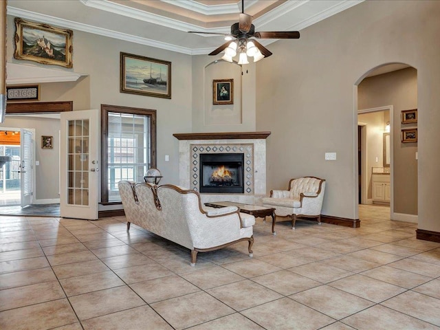 tiled living room with french doors, a fireplace, a raised ceiling, ornamental molding, and ceiling fan