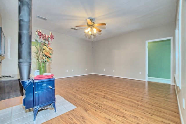 unfurnished room featuring light wood-type flooring, a wood stove, and ceiling fan