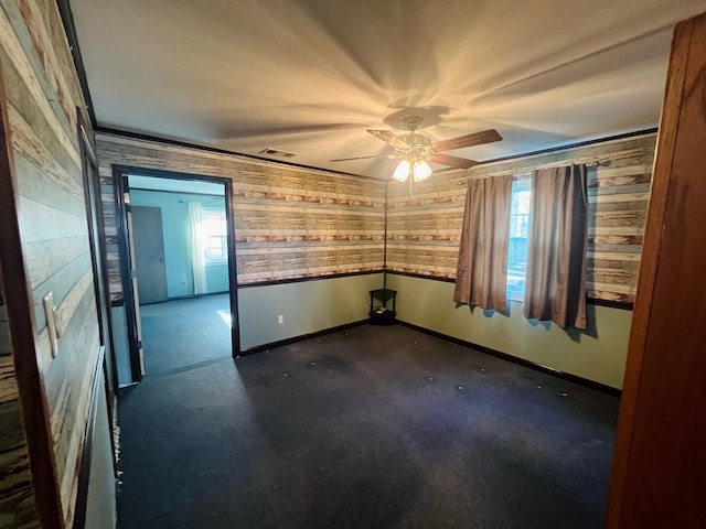 empty room featuring carpet floors, wood walls, and ceiling fan