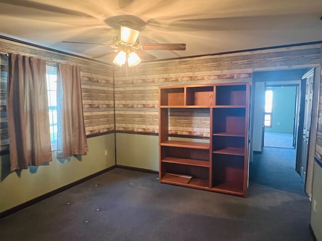 interior space with ceiling fan, wooden walls, and dark carpet