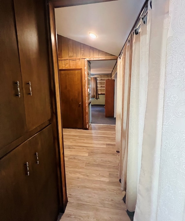 hallway with wooden walls, light hardwood / wood-style flooring, and lofted ceiling