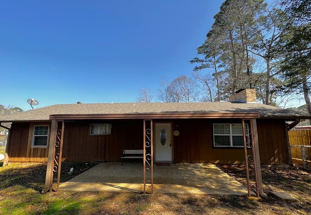 rear view of property with dirt driveway, fence, board and batten siding, a chimney, and a patio area