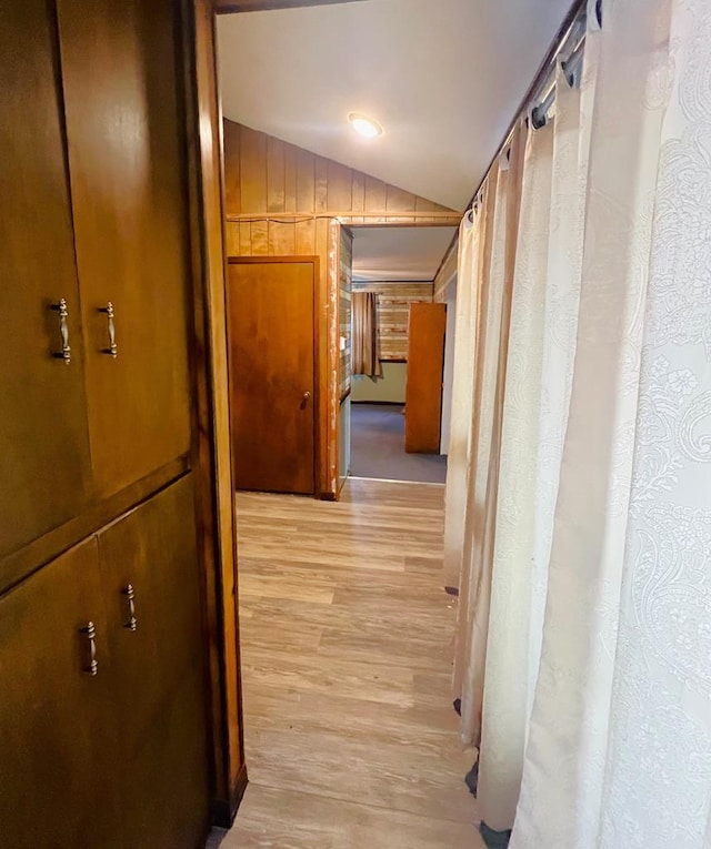 corridor with lofted ceiling, light wood-style floors, and wood walls