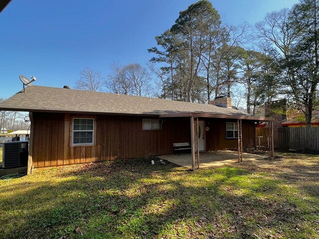 back of house with board and batten siding, fence, cooling unit, a chimney, and a patio area