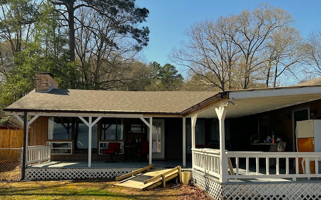 rear view of house featuring a chimney, a wooden deck, a shingled roof, and fence