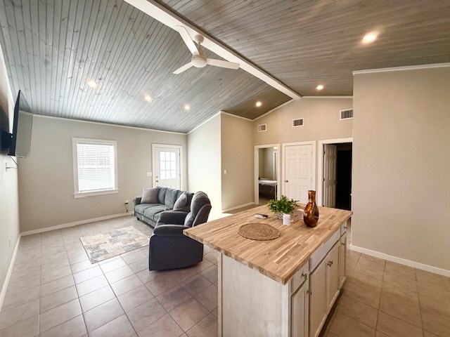 kitchen with light tile patterned floors, butcher block counters, lofted ceiling with beams, a kitchen island, and light brown cabinets