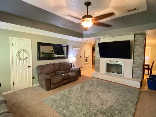 carpeted living room featuring ceiling fan, a brick fireplace, crown molding, and a raised ceiling