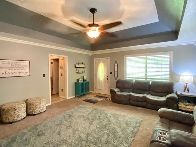 living room featuring ceiling fan, carpet, ornamental molding, and a tray ceiling