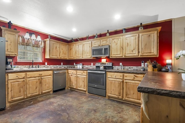 kitchen with a sink, a peninsula, stainless steel appliances, dark countertops, and concrete flooring