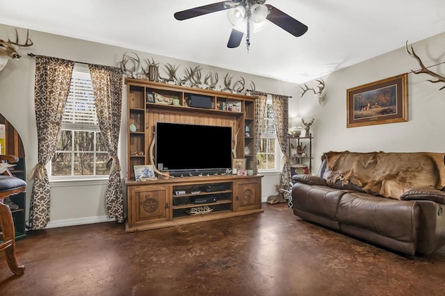 living room featuring baseboards, finished concrete flooring, a ceiling fan, and plenty of natural light