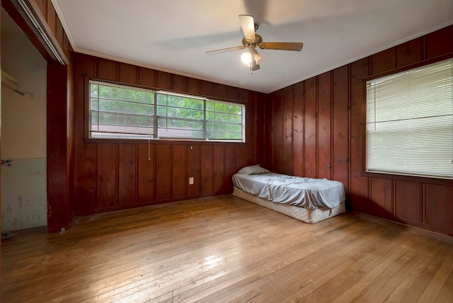 unfurnished bedroom with light wood-type flooring, ceiling fan, and wood walls