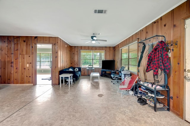 interior space with ceiling fan, ornamental molding, and wood walls