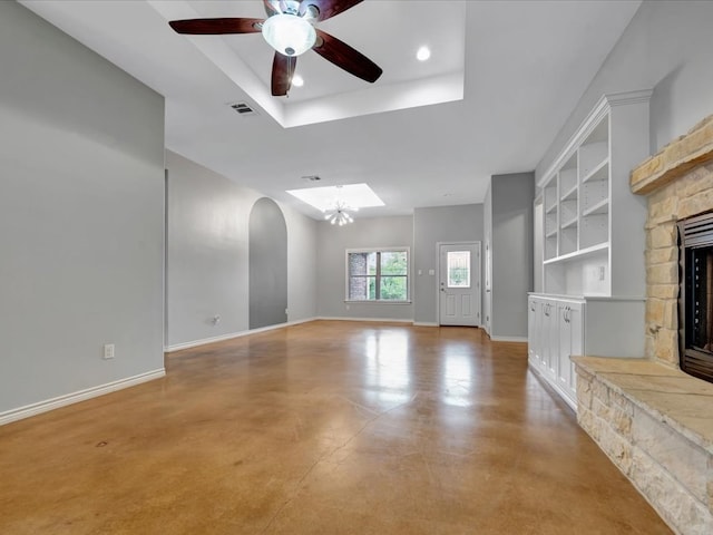 unfurnished living room featuring ceiling fan with notable chandelier, a raised ceiling, built in features, and a fireplace