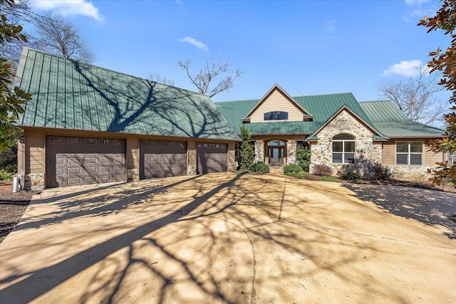 view of front of house featuring a garage, stone siding, metal roof, and driveway