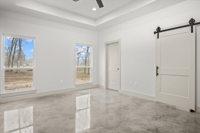 spare room featuring a tray ceiling, a barn door, and baseboards