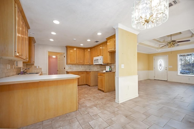 kitchen with sink, hanging light fixtures, kitchen peninsula, ceiling fan with notable chandelier, and ornamental molding