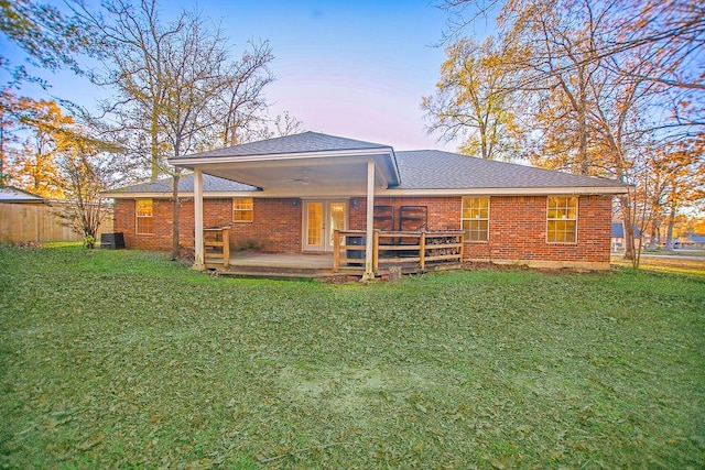 back house at dusk with central AC unit, a patio area, and a lawn