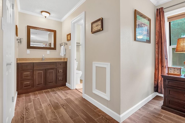 bathroom featuring wood finished floors, vanity, baseboards, toilet, and ornamental molding