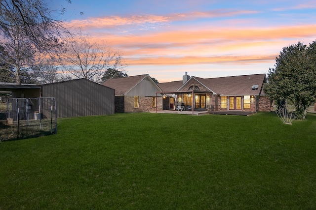 back house at dusk featuring a lawn and a patio