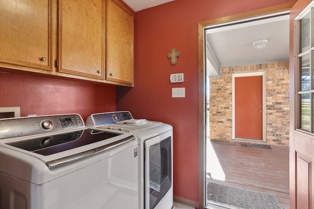 laundry room featuring brick wall, washer and dryer, and cabinets