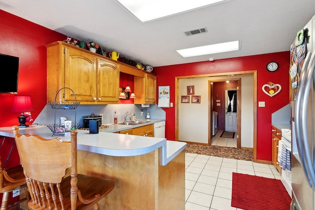 kitchen with kitchen peninsula, sink, white dishwasher, a breakfast bar area, and light tile patterned floors