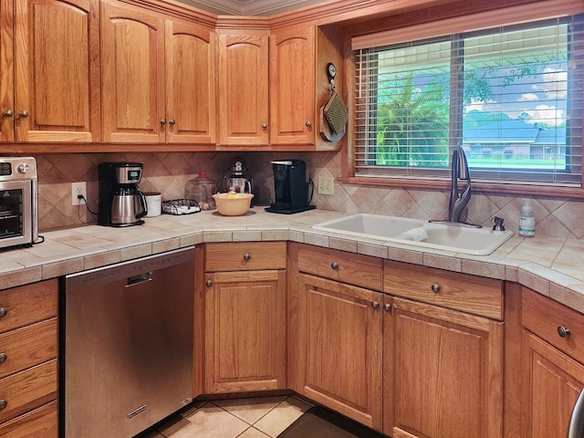 2104 Pinecrest Dr, Jasper, TX 75951 - kitchen featuring stainless steel dishwasher, backsplash, light tile patterned floors, tile countertops, and brown cabinetry